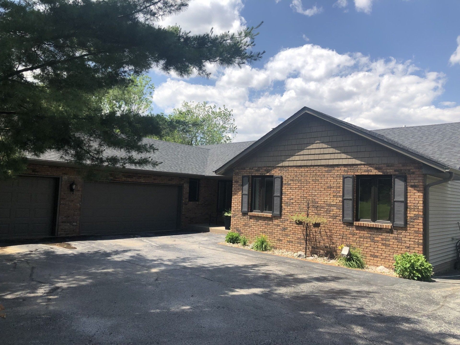 Brick house with a two-car garage, asphalt driveway, and blue shutters.