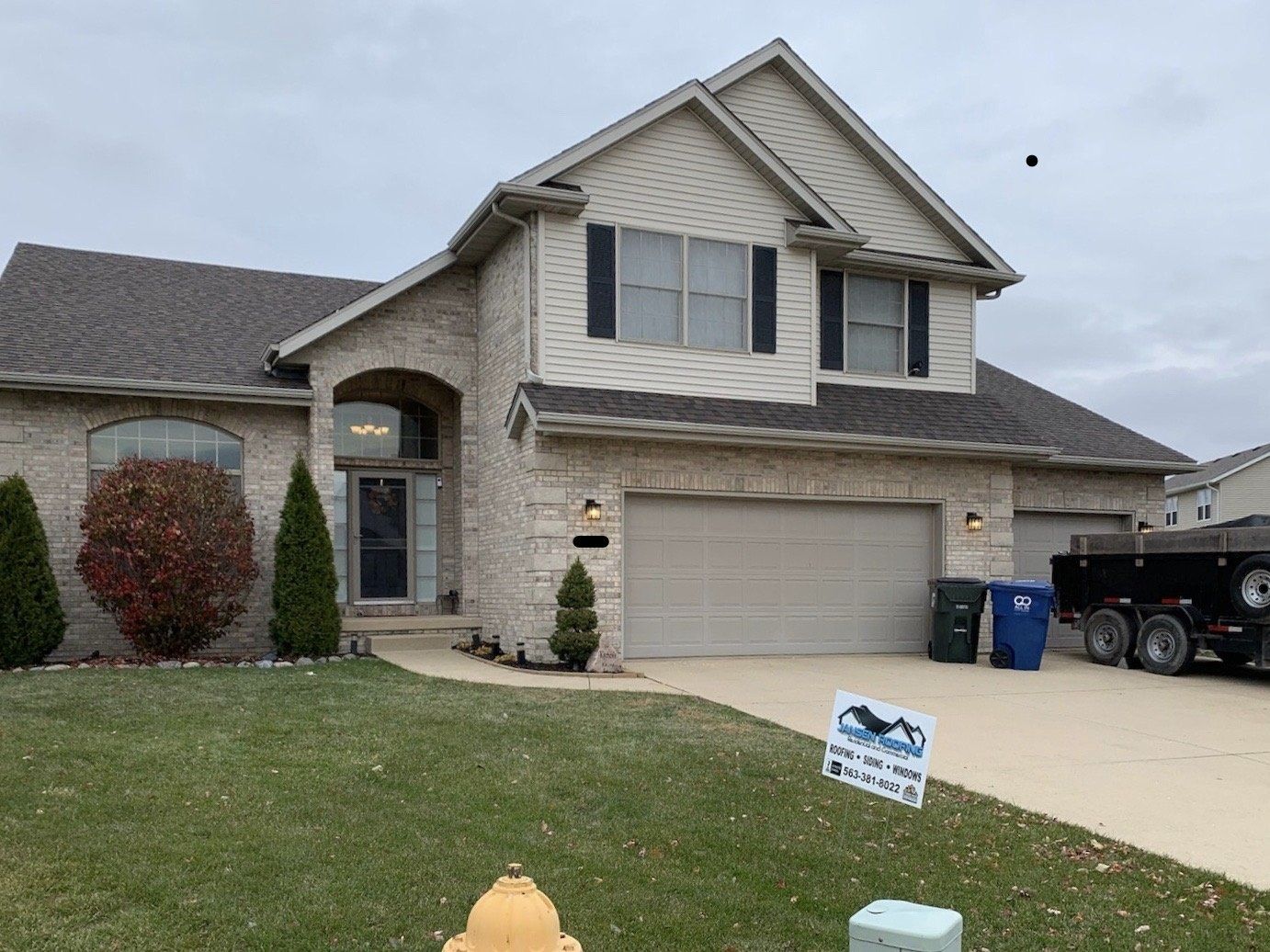 Two-story brick house with a dark roof and a two-car garage. A sign sits in the yard.