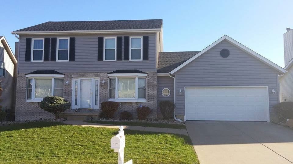 Two-story house with gray siding, black shutters, white garage door, and a green lawn.