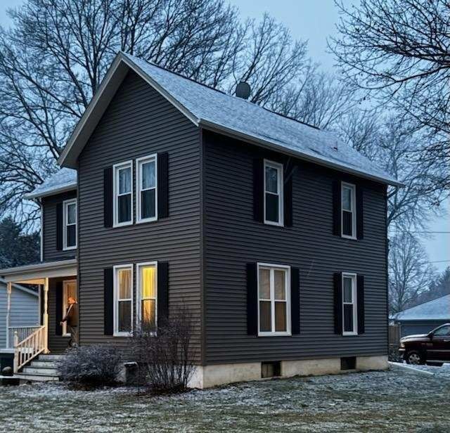 Two-story gray house with black shutters, snow on the roof, and bare winter trees.