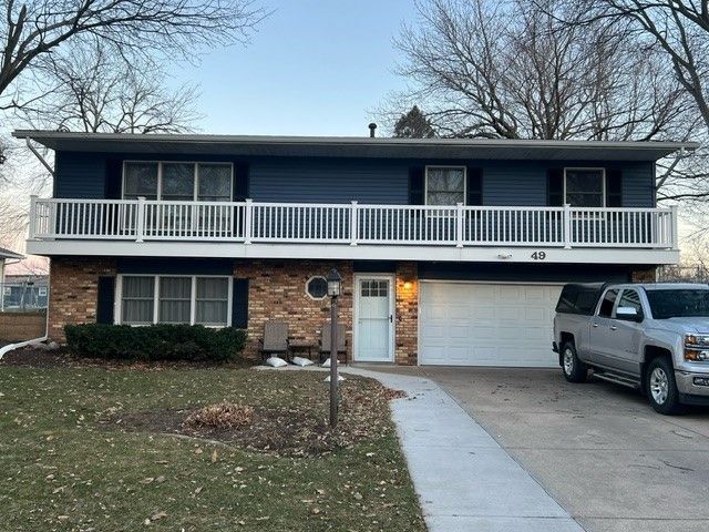 Two-story house with a blue upper level and a brick lower level. A white railing surrounds a balcony. A truck is parked in the driveway.