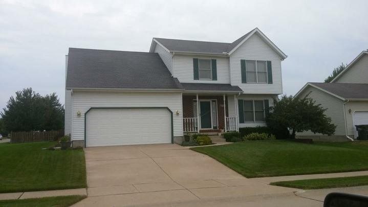 White two-story house with a two-car garage, green shutters, and a well-manicured lawn on a cloudy day.