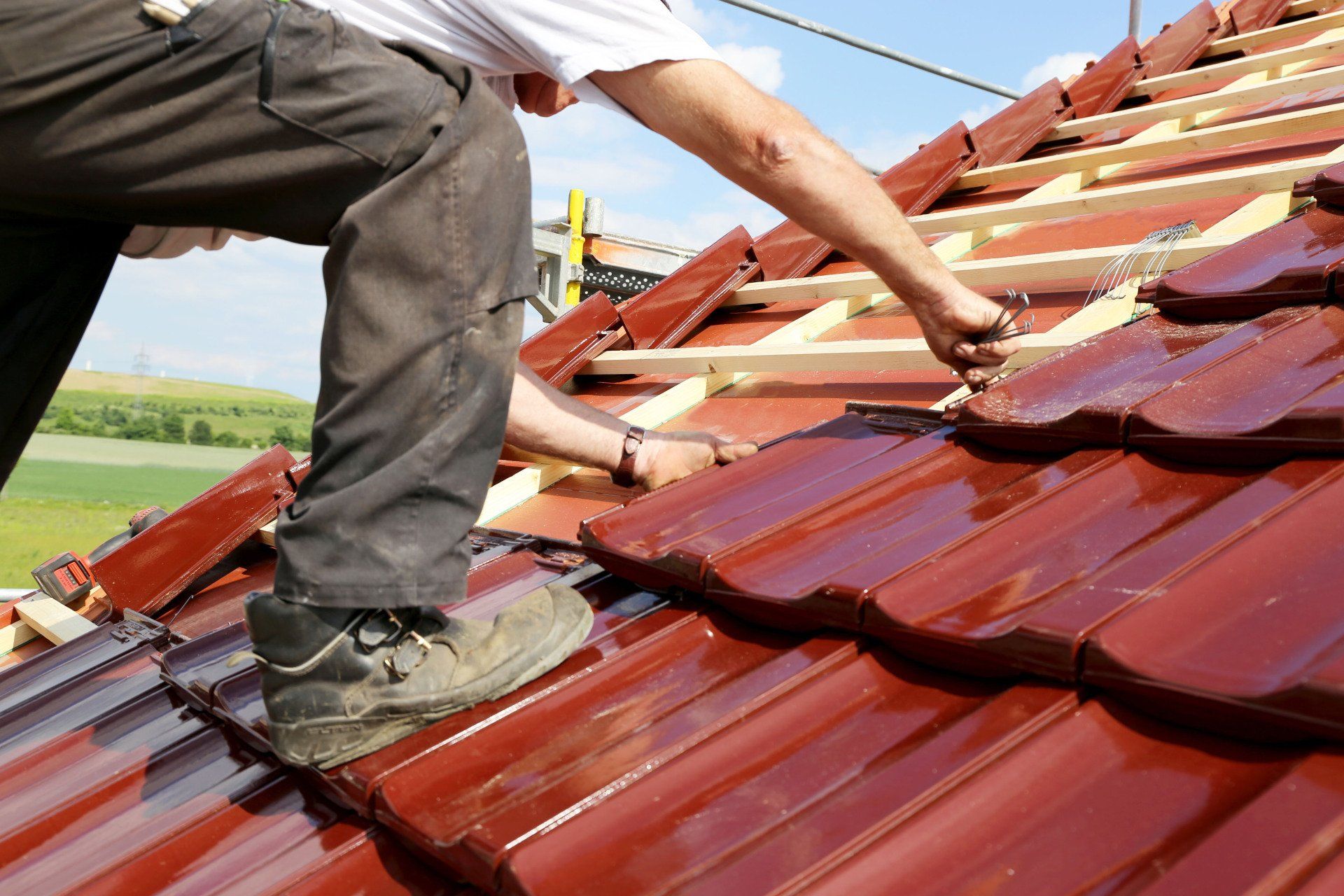 Roofer installing red tiles on a roof, using a tool.