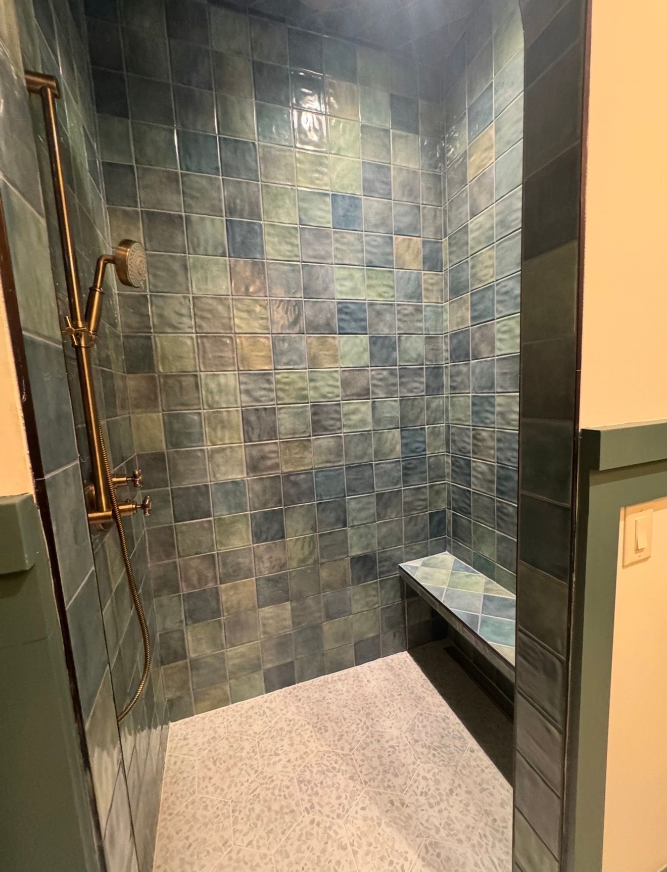 Small tiled walk-in shower with blue-gray walls, light floor, and built-in bench.