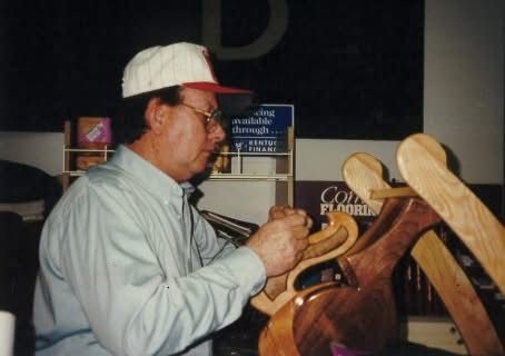 Man in a white cap examining wooden sculpture at an indoor craft display