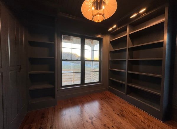 Empty walk-in closet with dark built-in shelves, wood floor, and a window with natural light