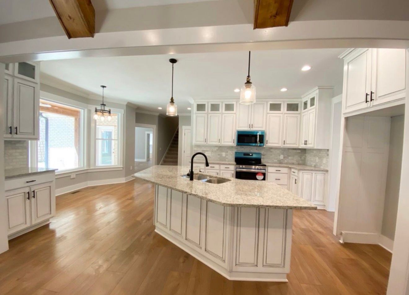 Bright white kitchen with wood floors, marble island, pendant lights, and built-in cabinets