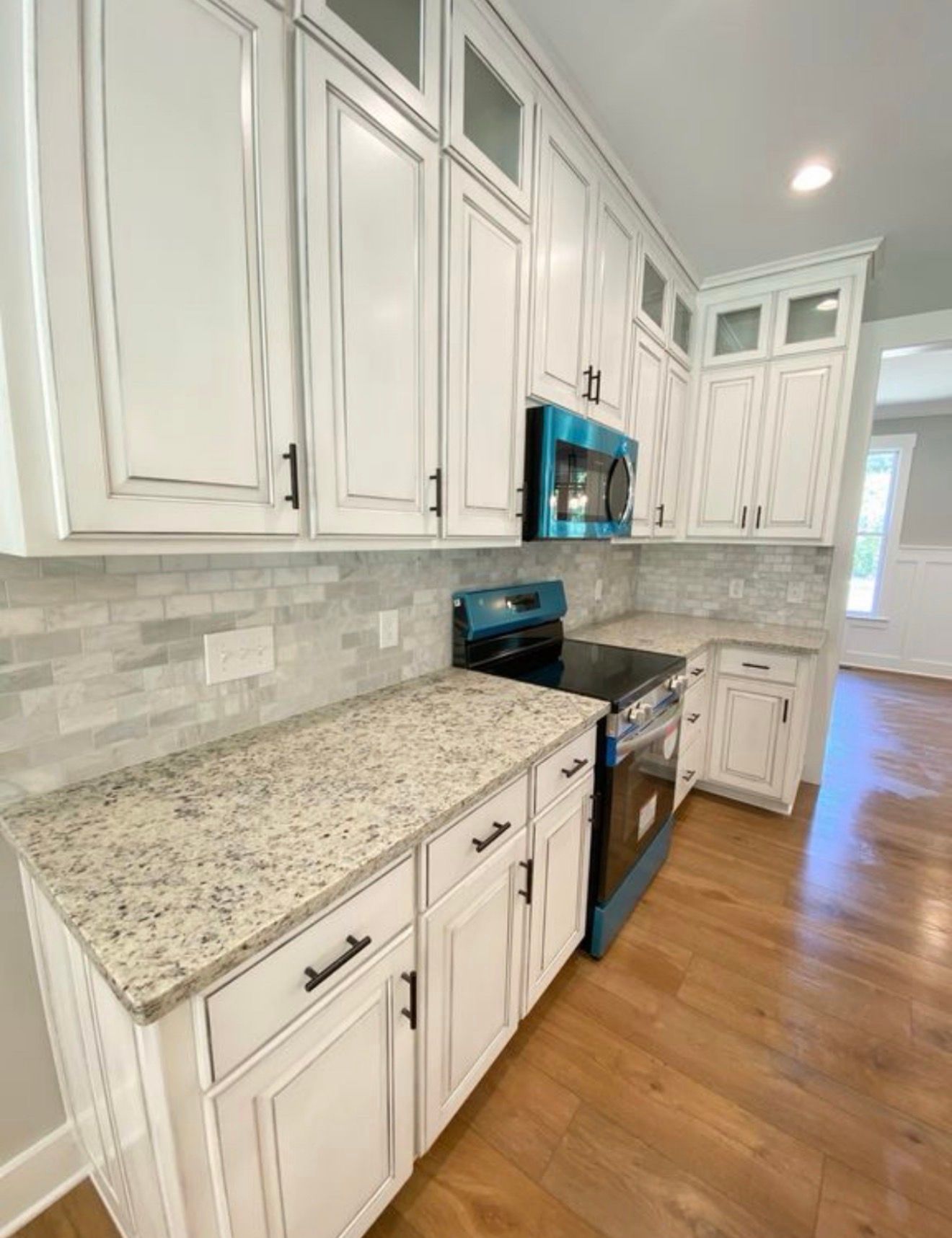 Bright white kitchen with granite countertops, stainless stove, and wood floors