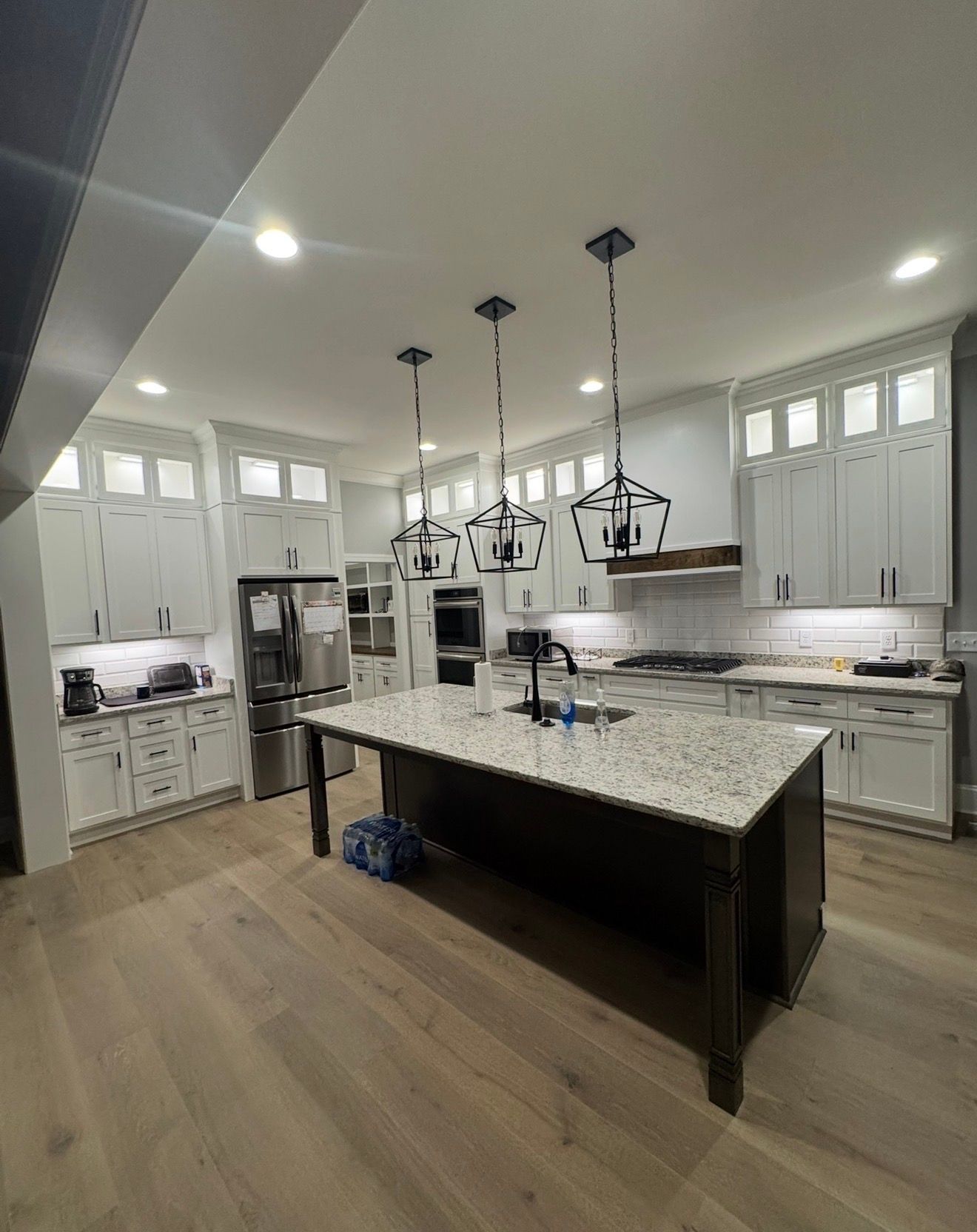 Modern white kitchen with a large island, pendant lights, and light wood floors