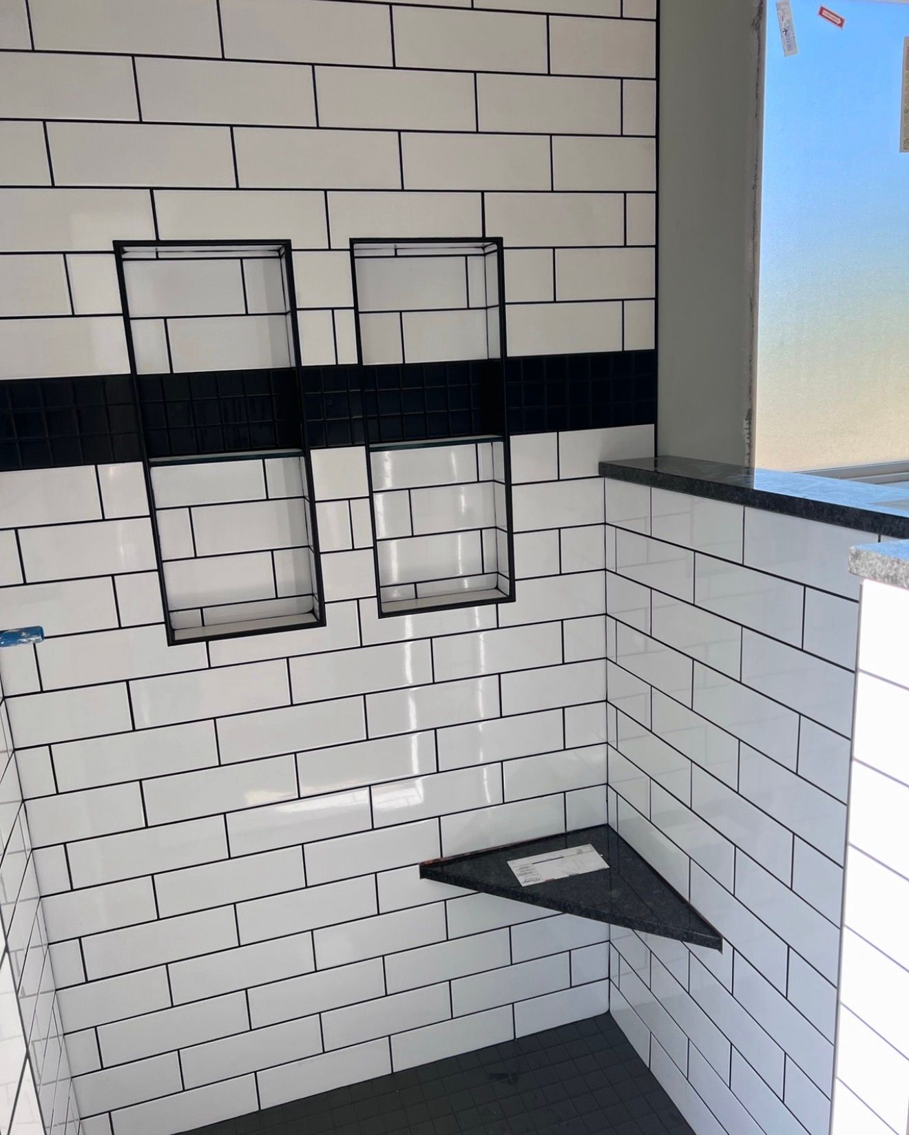 White tiled restroom corner with two wall-mounted mirrors and a triangular sink by a window.