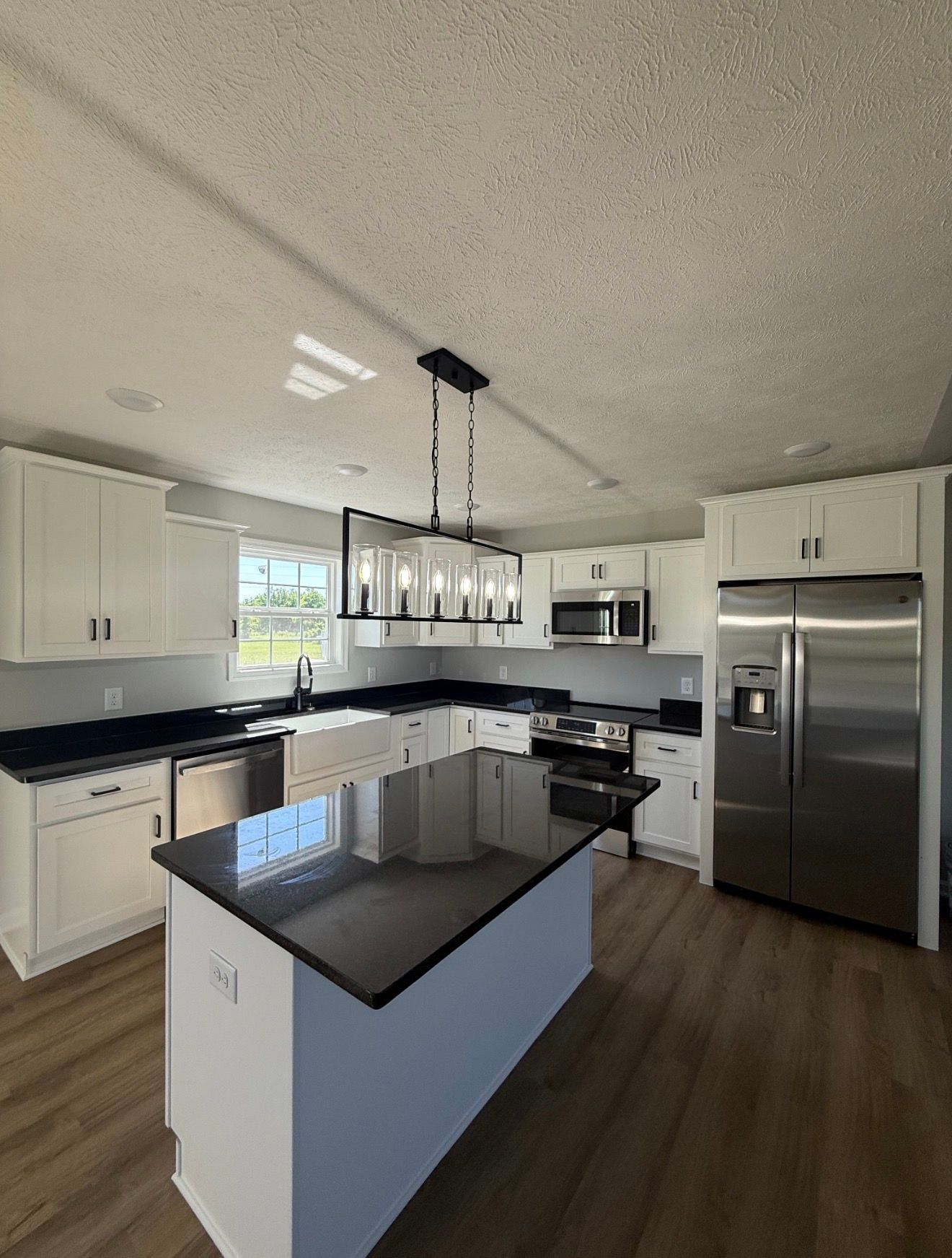 Bright modern kitchen with white cabinets, black countertops, central island, and stainless steel appliances.