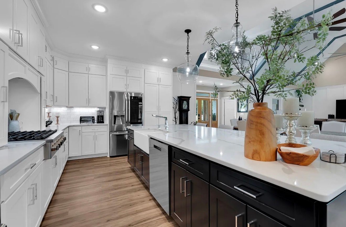 Bright modern white kitchen with black island, wood floors, and large vase centerpiece