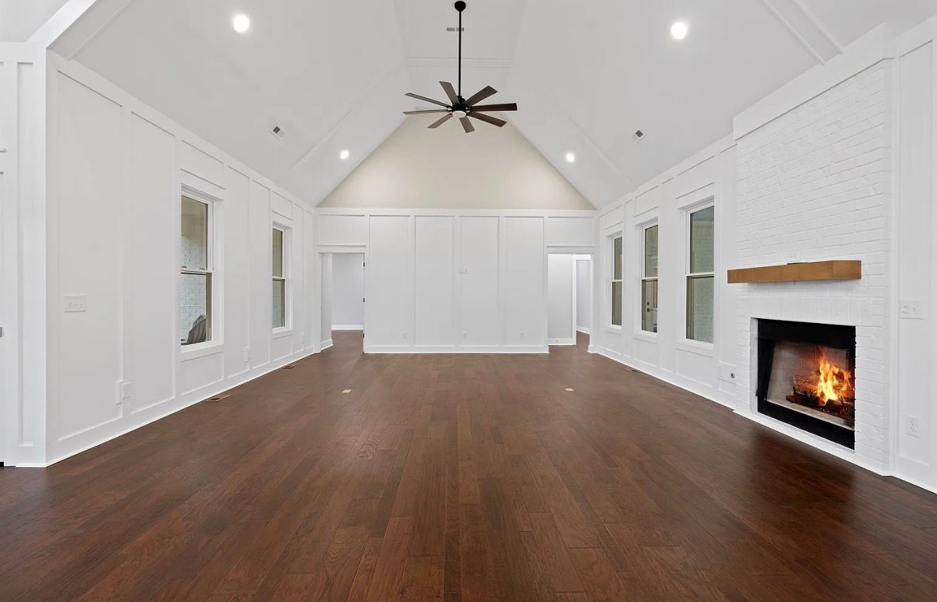 Spacious white living room with hardwood floors, vaulted ceiling, ceiling fan, and fireplace