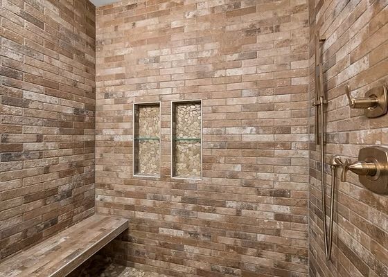 Stone-tiled shower with two narrow windows, bench, and brass shower fixtures