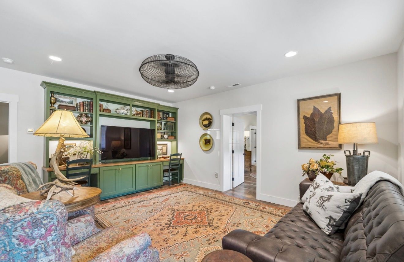 Bright living room with green TV cabinet, patterned rug, sofa, lamps, and wall art