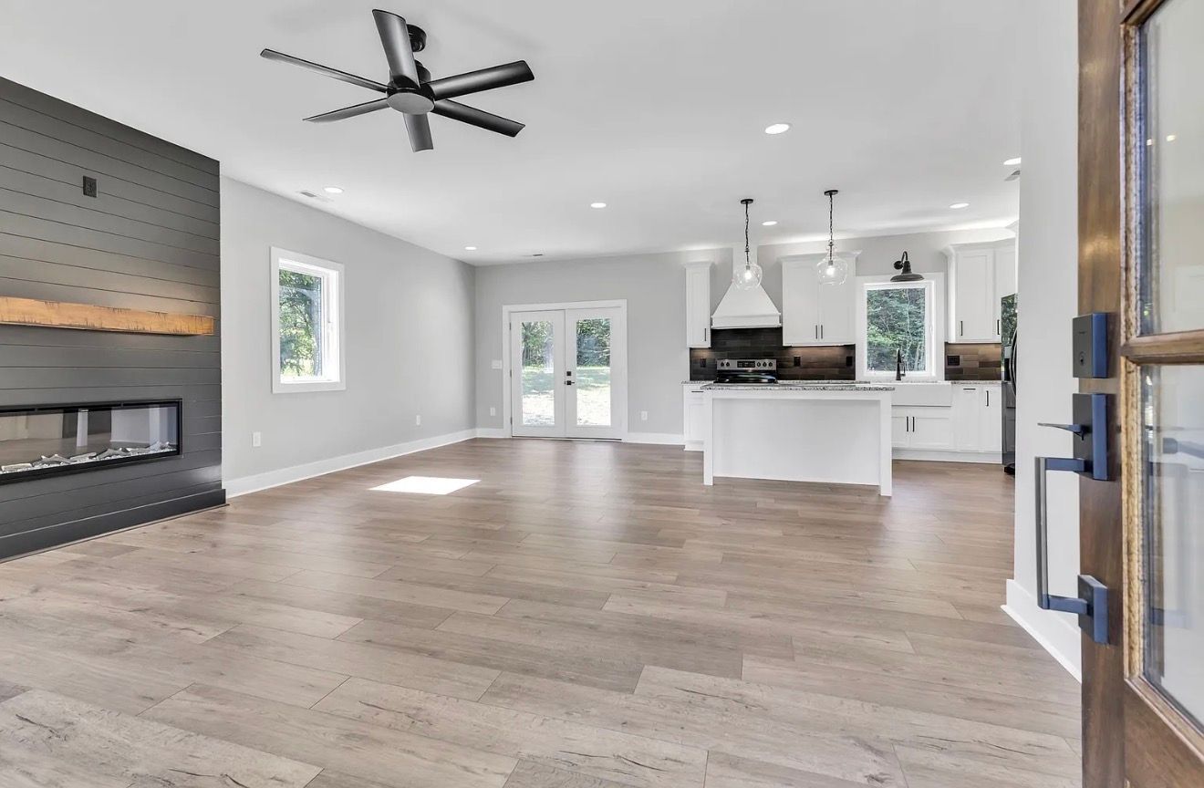 Bright open living room with fireplace, ceiling fan, white kitchen island, and hardwood floors