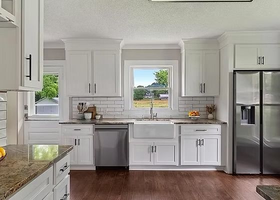 Bright white kitchen with stainless steel appliances, dark wood floors, and a window over the sink
