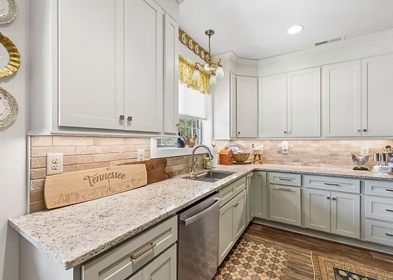 Bright modern kitchen with light gray cabinets, granite counters, stainless dishwasher, and patterned rug.
