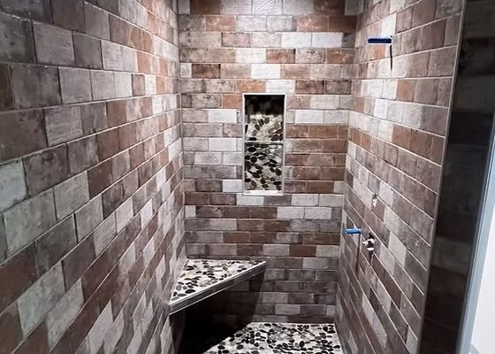 Small tiled bathroom with a shower, built-in bench, and wall niche in brown and beige tones