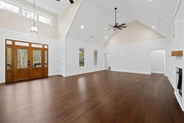 Spacious living room with vaulted ceiling, wood floors, large windows, and double wooden doors