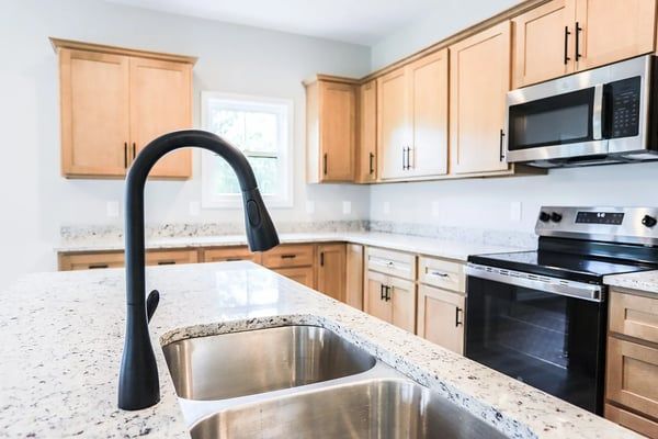 Bright modern kitchen with light wood cabinets, stainless appliances, and a black faucet over a marble island sink.