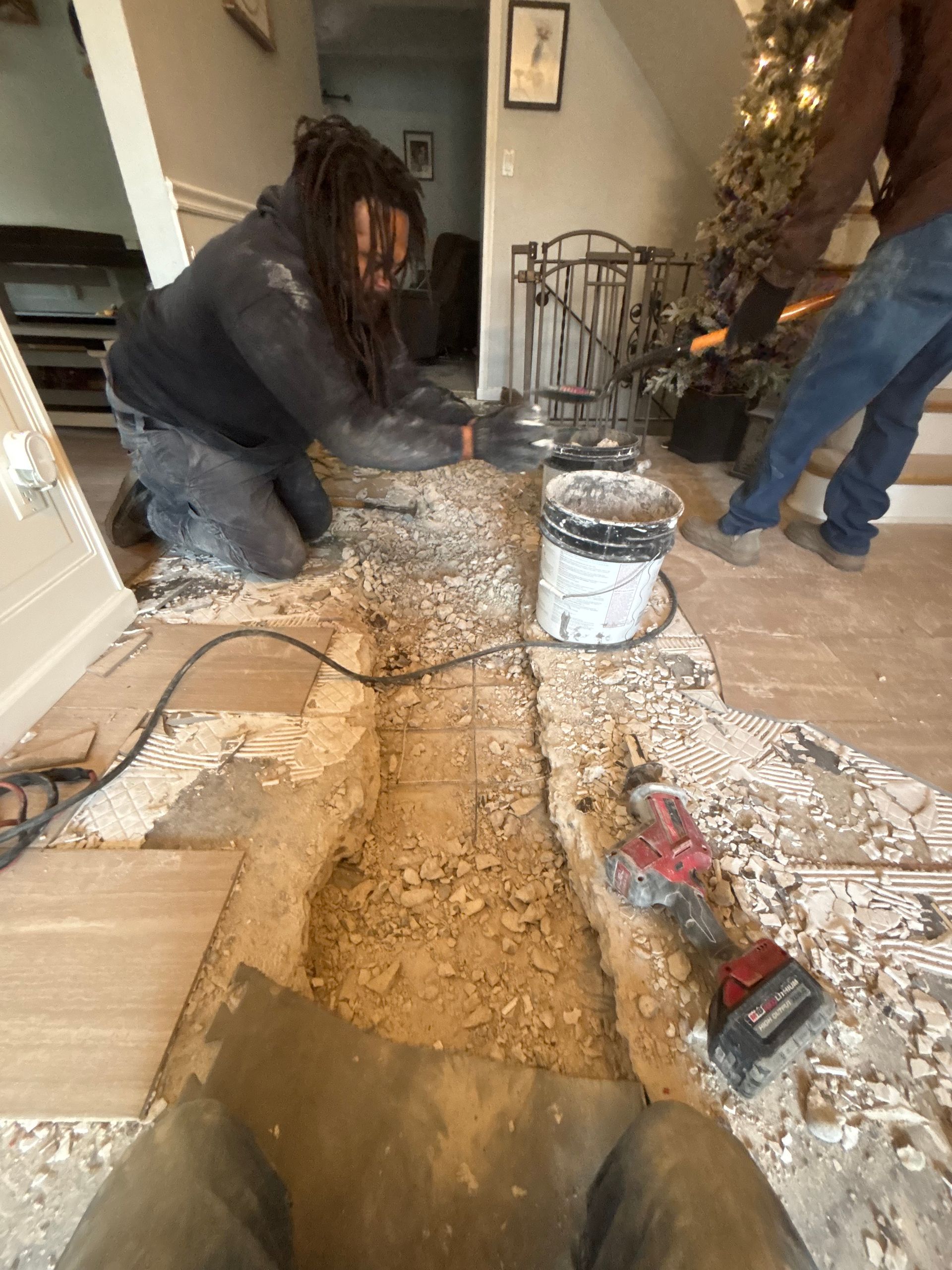 Two people working on floor demolition indoors, debris scattered. One kneels, focused.  A power tool sits nearby.