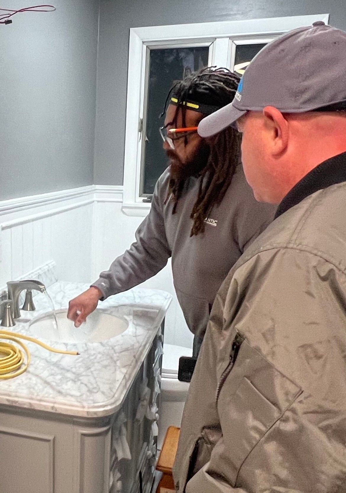 Two men examining a bathroom sink during a home renovation. One points to the sink.