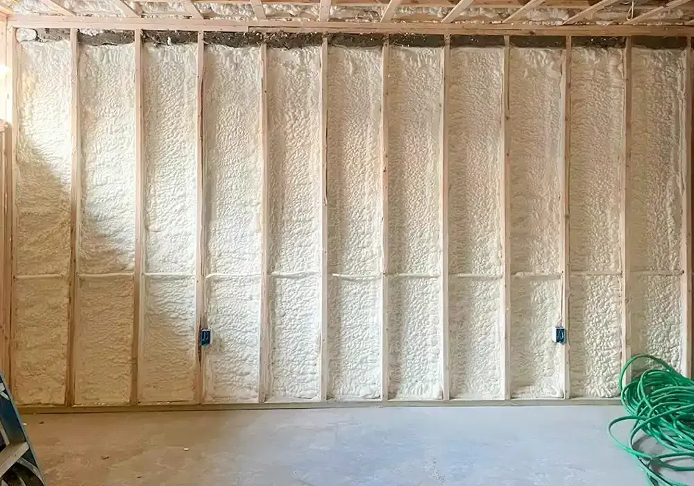 A room with a wall covered in spray foam and a green hose.