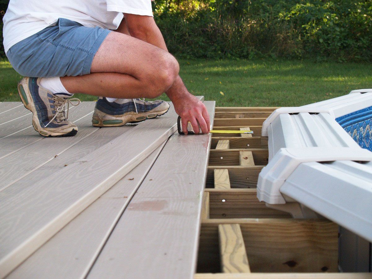 Person measuring a deck board on a partially built wooden deck outside.