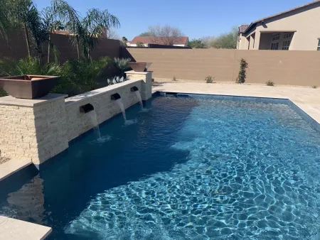 Pool with water cascading from stone wall into blue water, against a neutral wall backdrop.