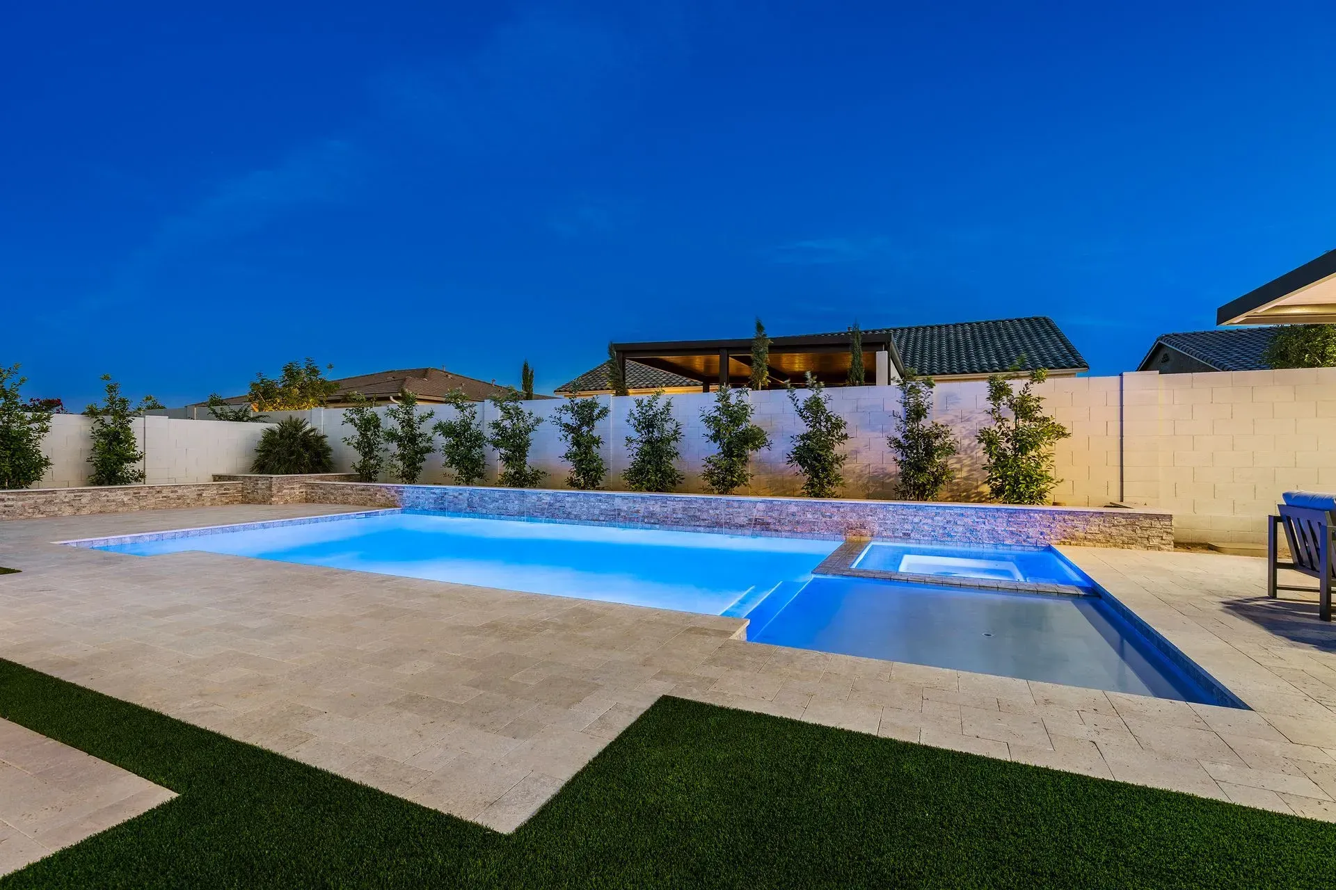 Pool with blue water and surrounding patio at night. Artificial grass border.