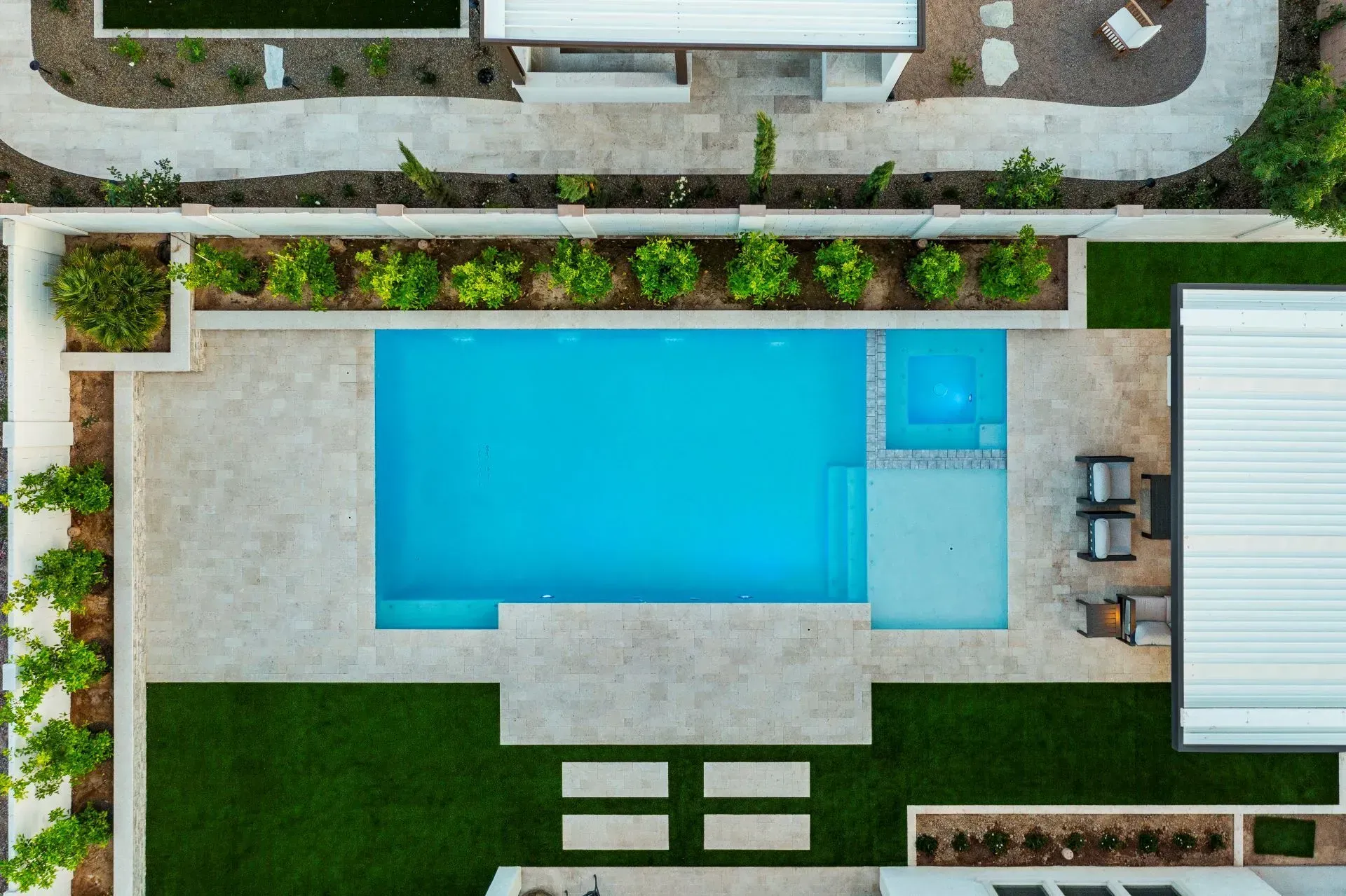 Aerial view of a rectangular pool with a spa, surrounded by travertine, landscaping, and a grassy area.