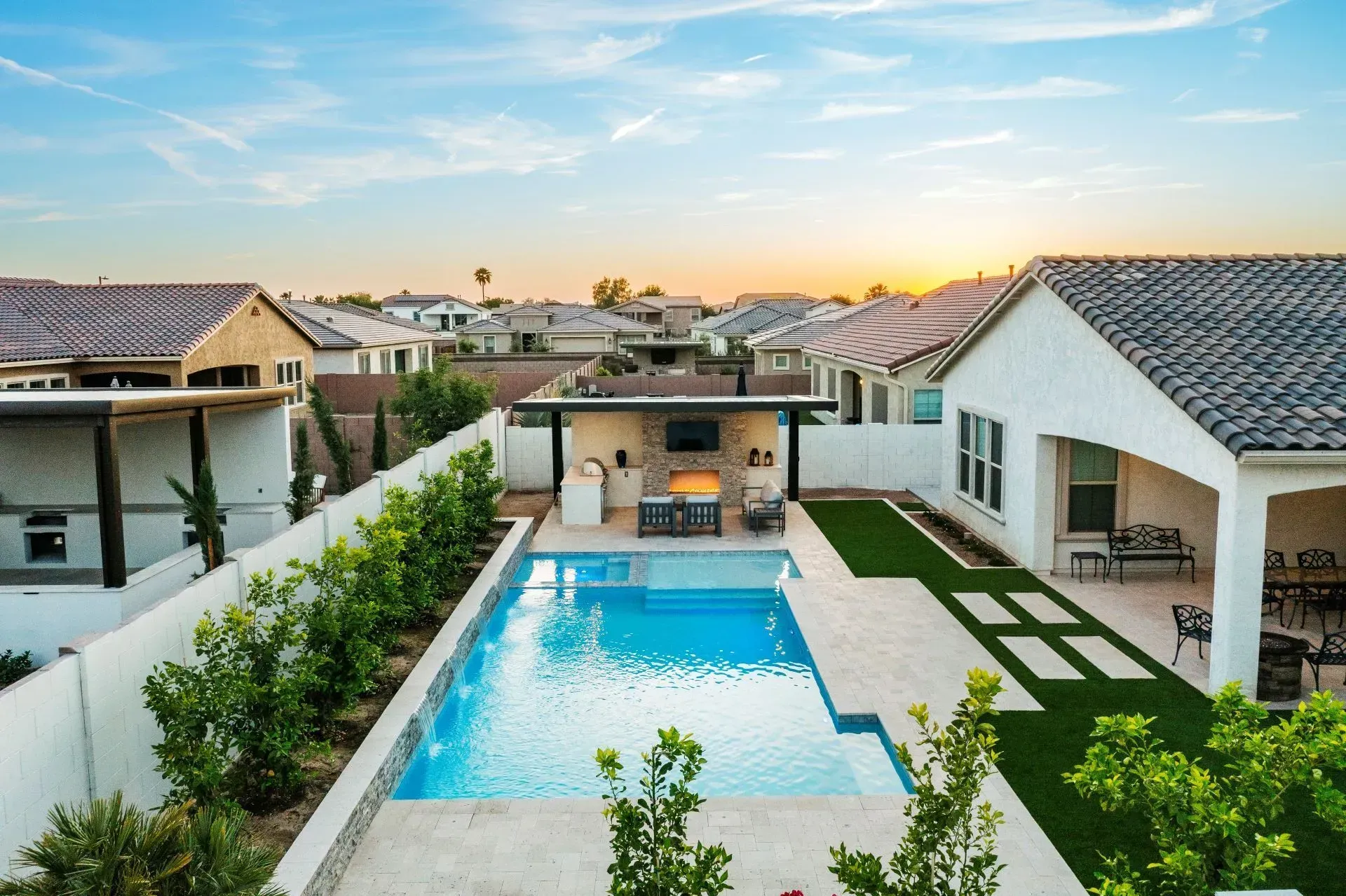 Backyard pool with outdoor kitchen, landscaping, and adjacent home.