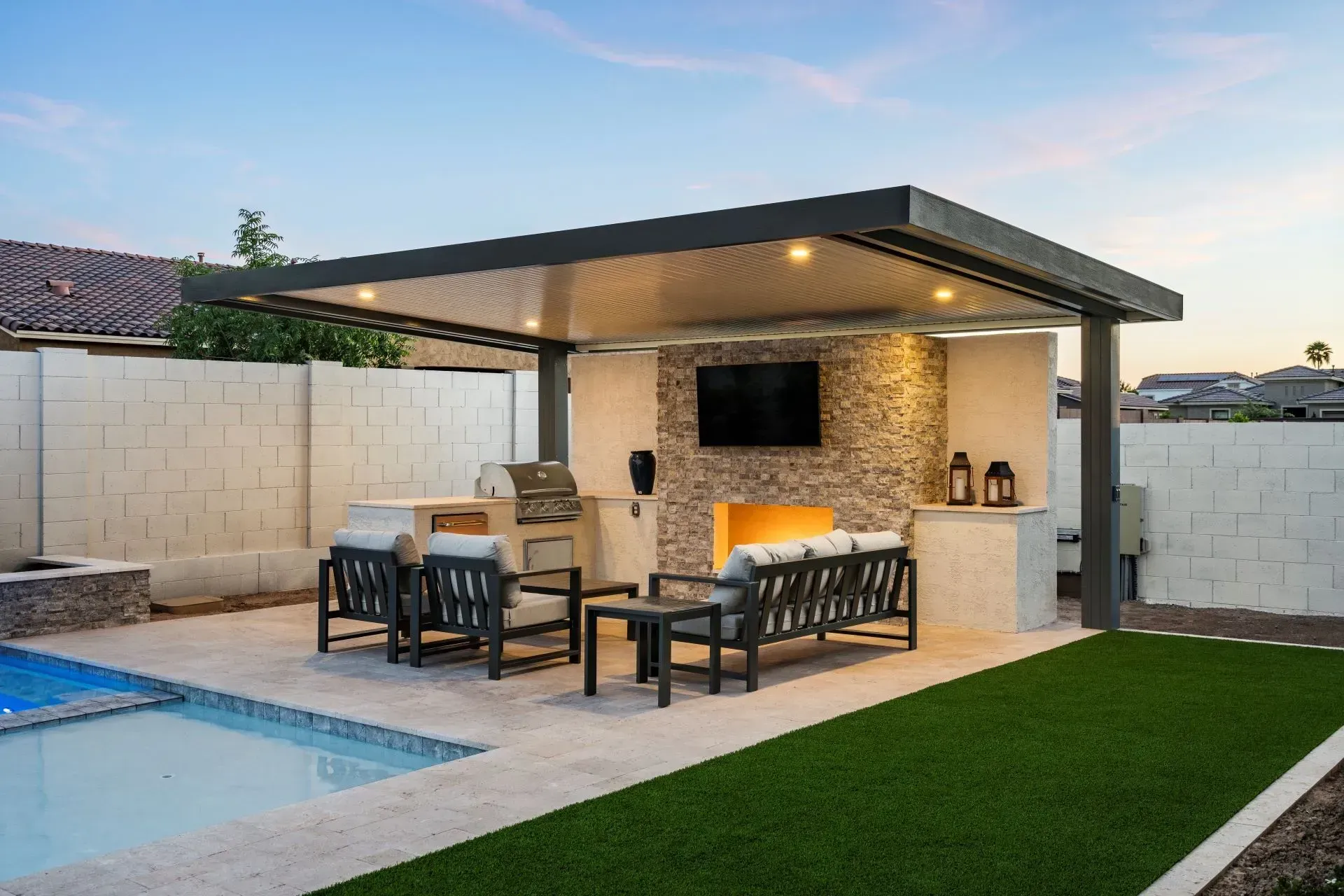 Outdoor patio with a pool and covered seating area, fireplace, and grill.
