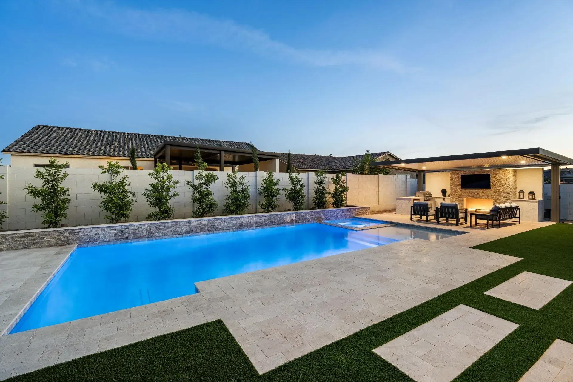 Pool and outdoor kitchen in a backyard with blue pool water and green artificial grass.