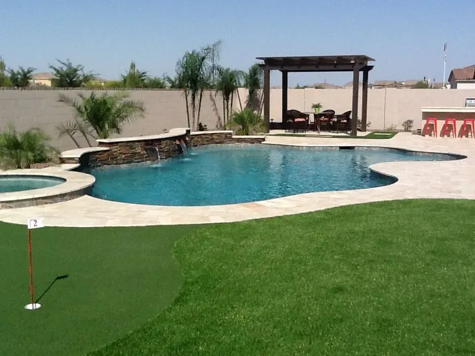 Backyard with pool, putting green, pergola, and bar, all set against a neutral wall.