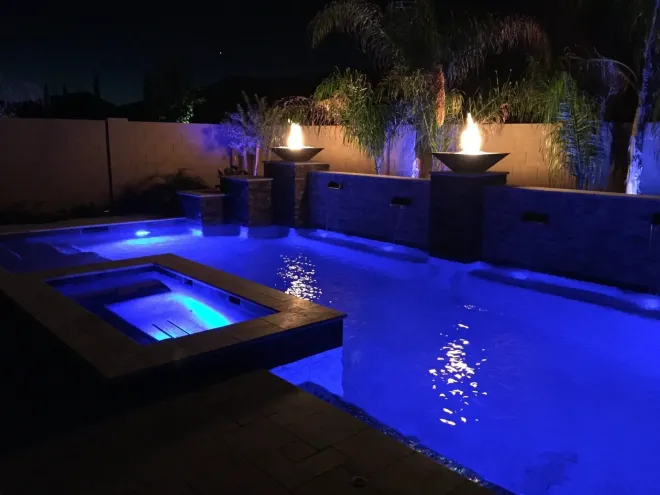 Nighttime pool with blue lights and fire features.