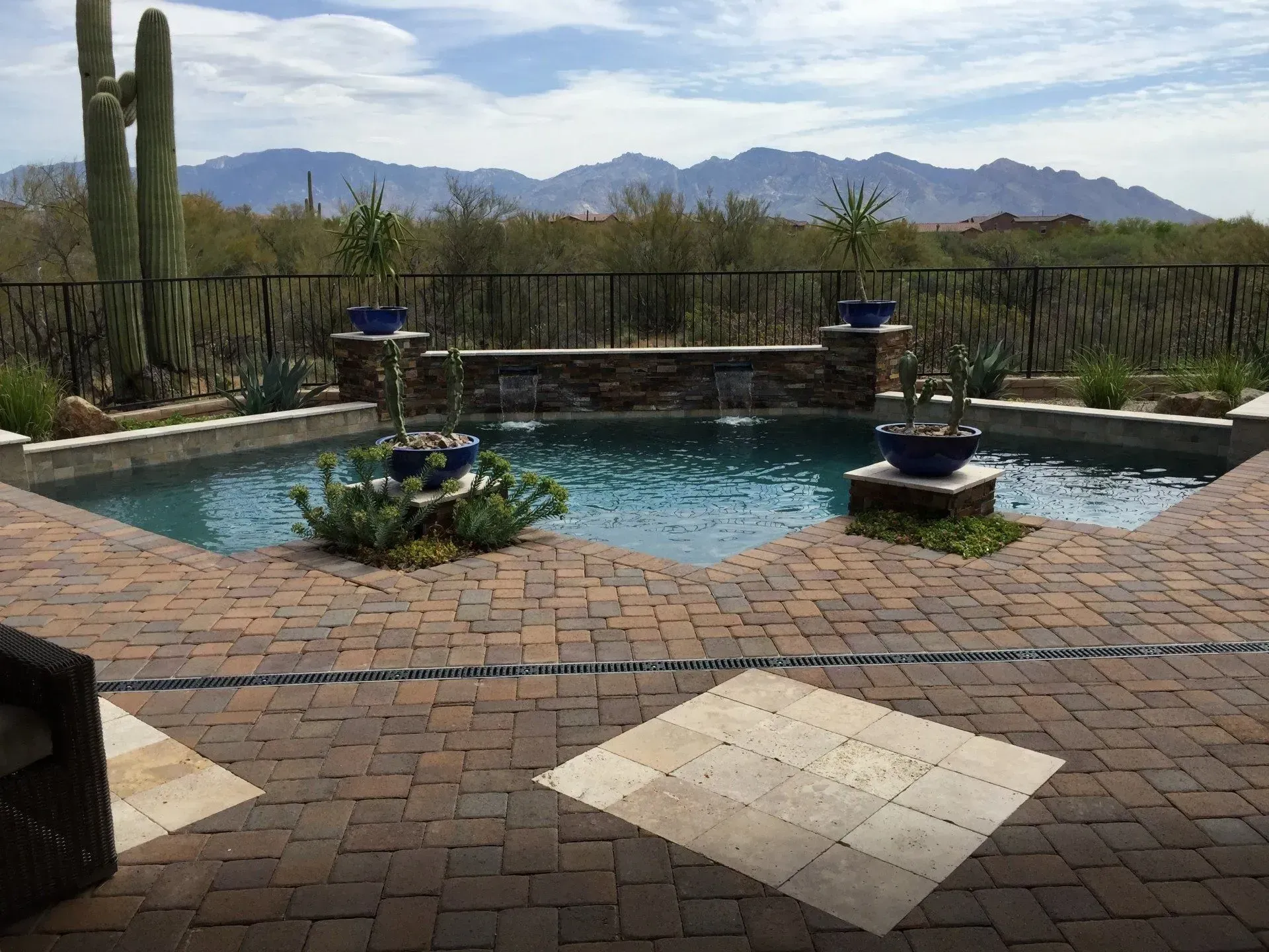 Pool with brick patio, water features, desert plants, and mountain view under blue sky.