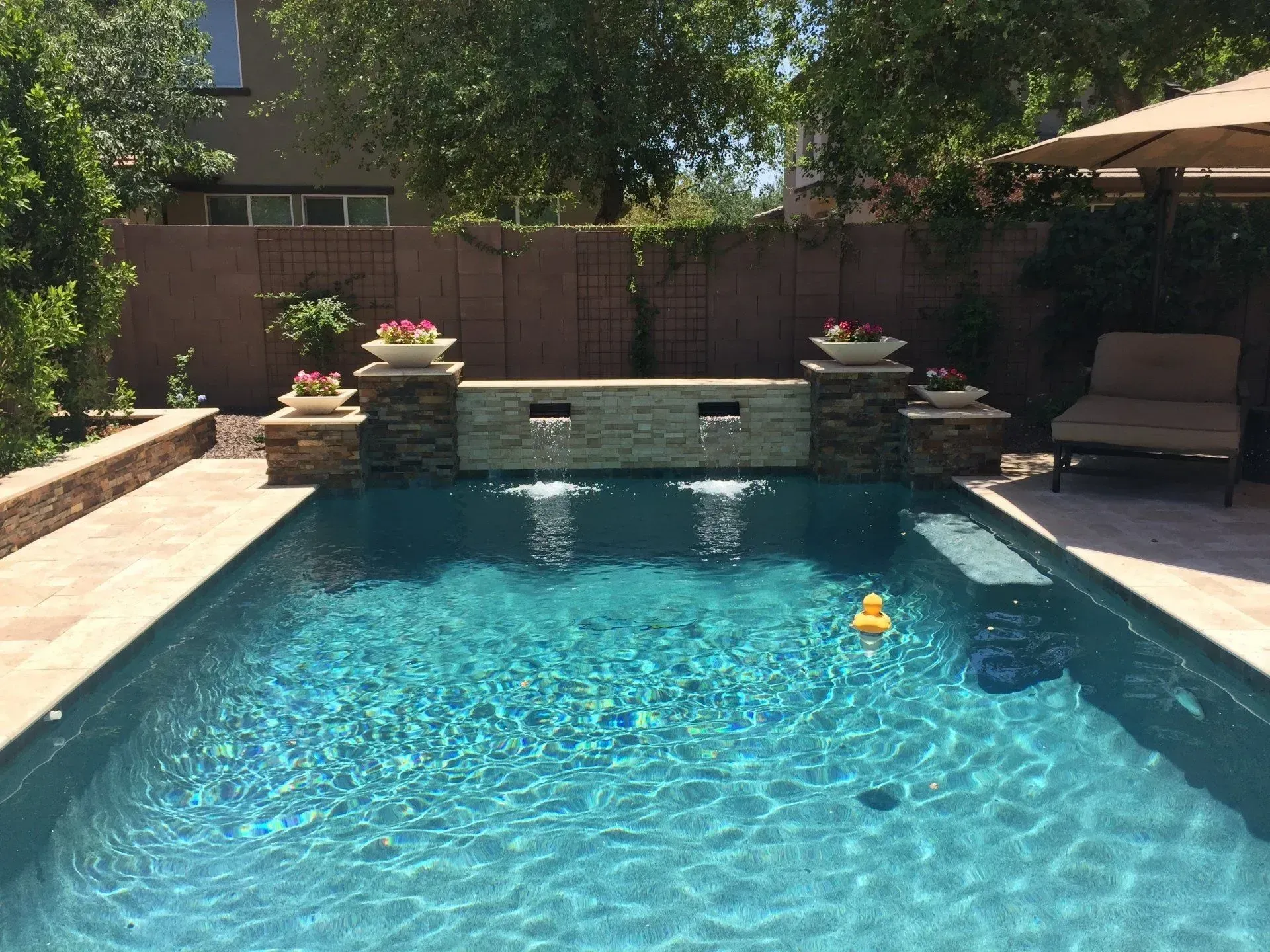 A rectangular swimming pool with blue tiles, stainless steel ladder, and beige poolside, in front of a building.