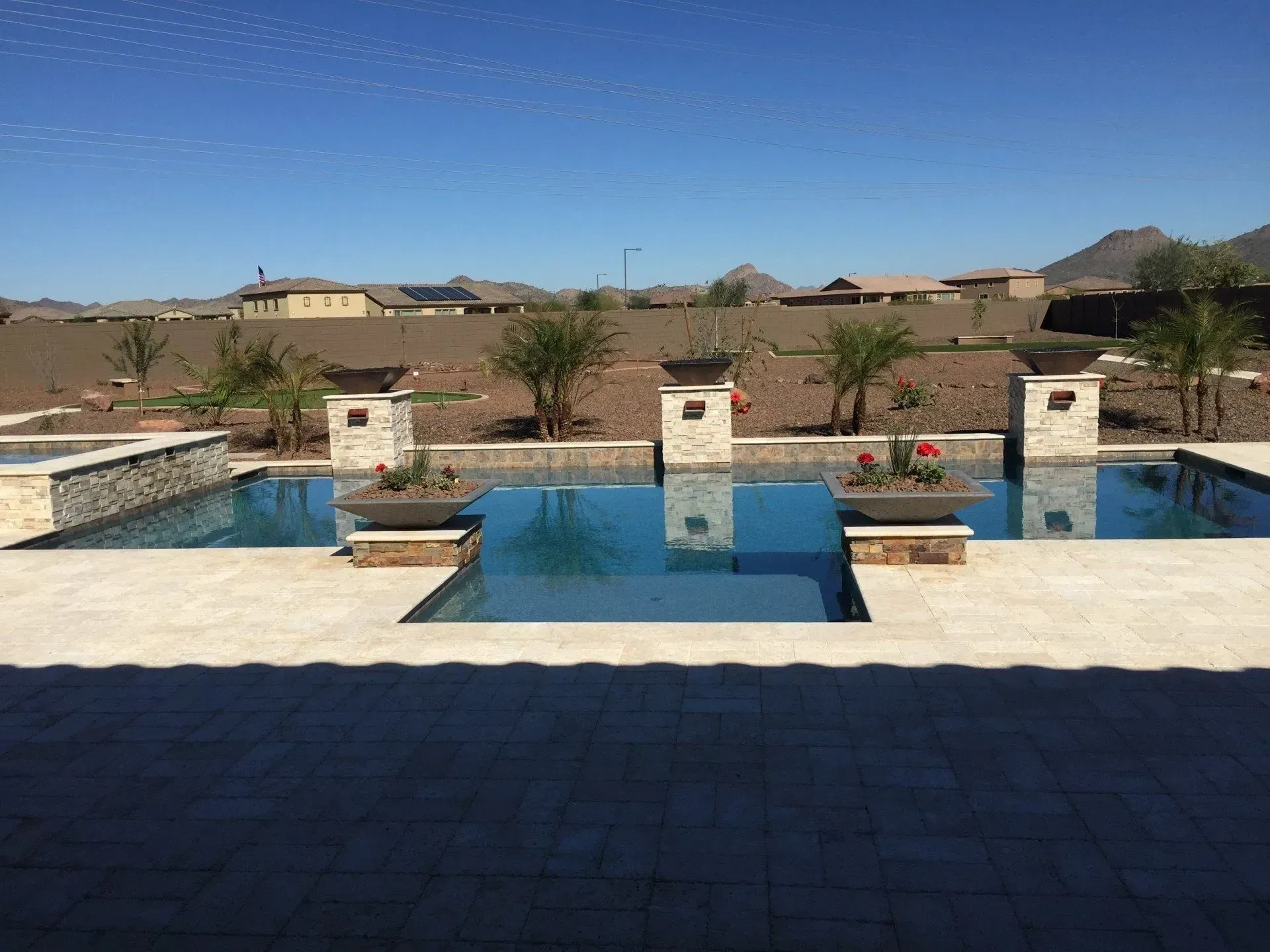 Three connected swimming pools on a sunny day with potted plants and background hills.