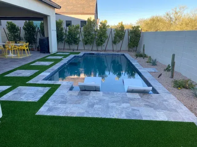 Rectangular pool with gray tile surround, green turf, and lounge chairs. Bamboo in background.