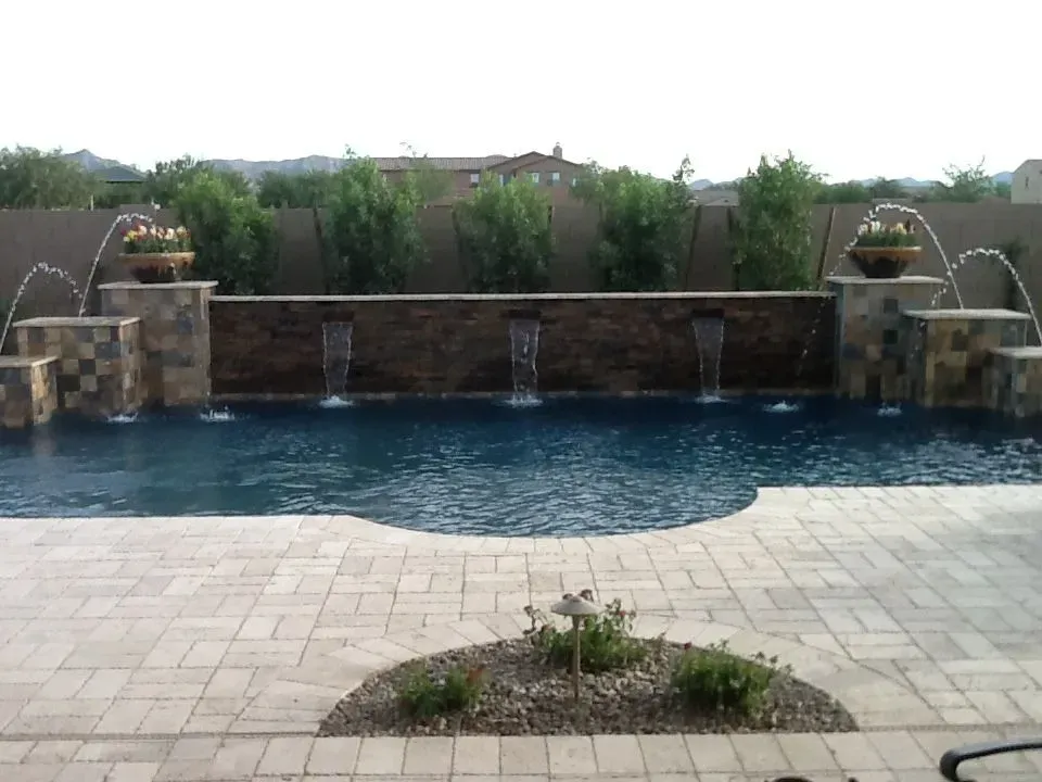 Swimming pool with cascading waterfalls, stone wall, and landscaping in a backyard setting.