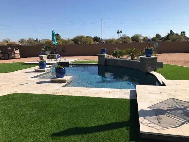 Backyard pool with turquoise umbrella, blue pots, stone accents, and artificial green grass.