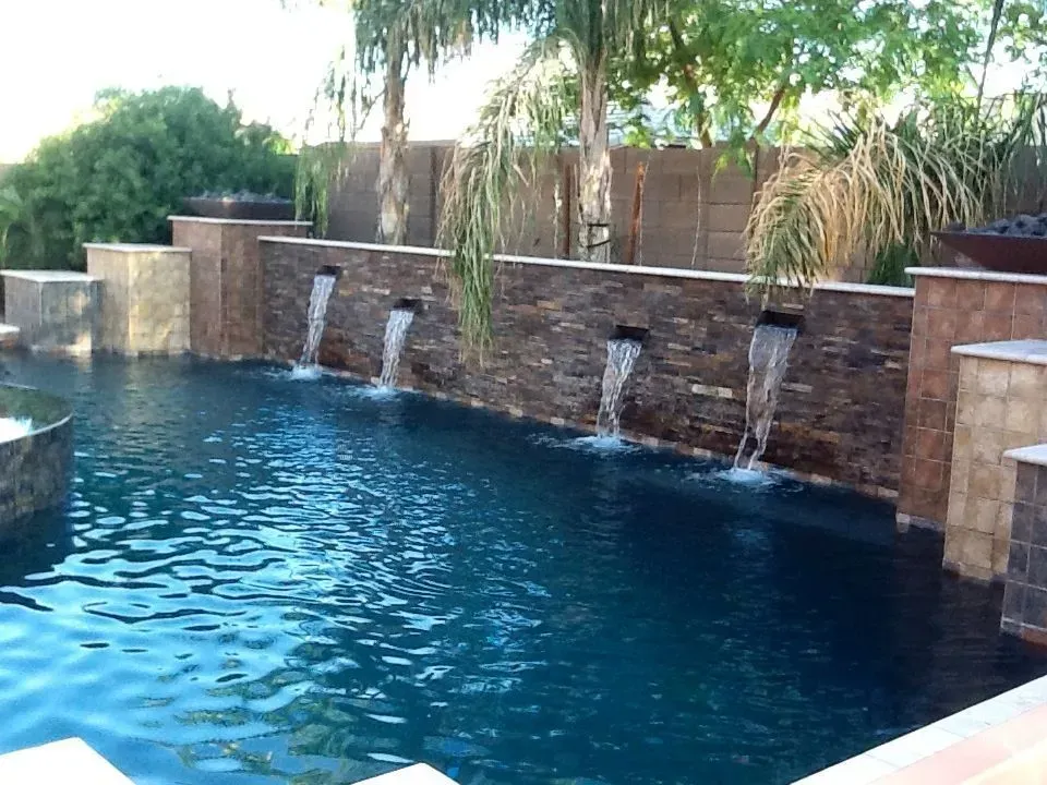 Pool with stone wall and water features, water flowing from spouts into pool.