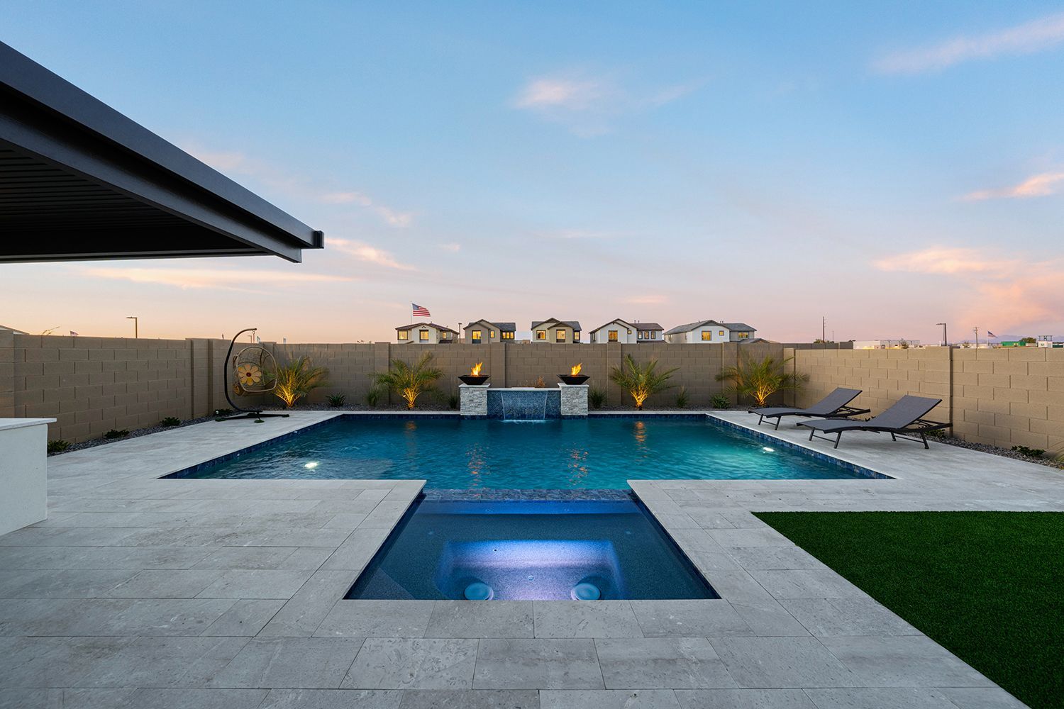 Pool and spa in a backyard with landscaping, fire features, and lounge chairs; evening.