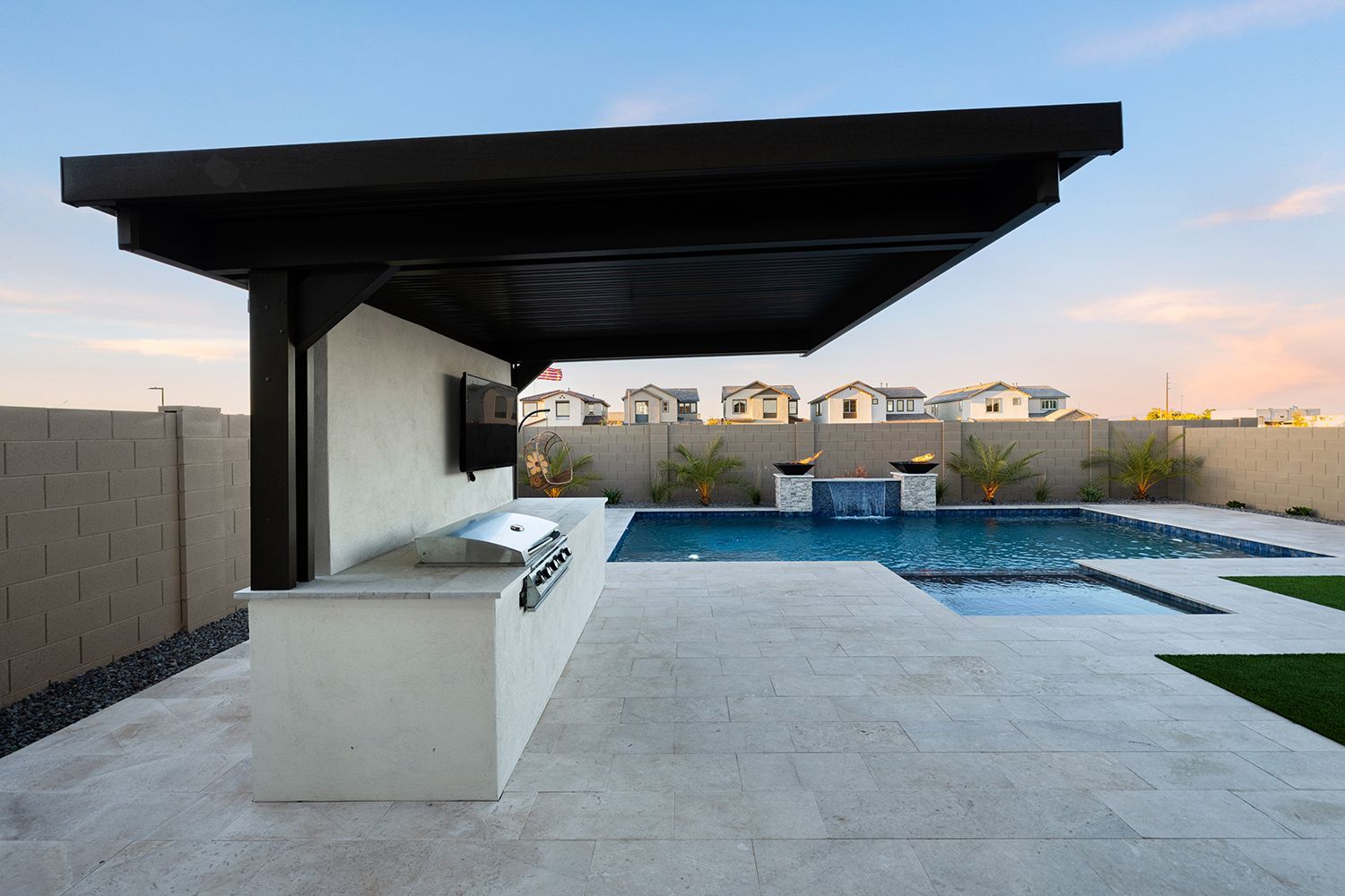 Outdoor kitchen with a grill, pool, and pergola with a television.