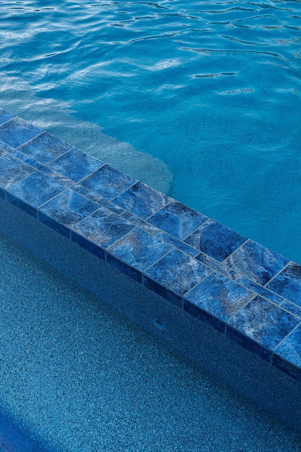 Blue tiled steps descending into a pool of rippling turquoise water.