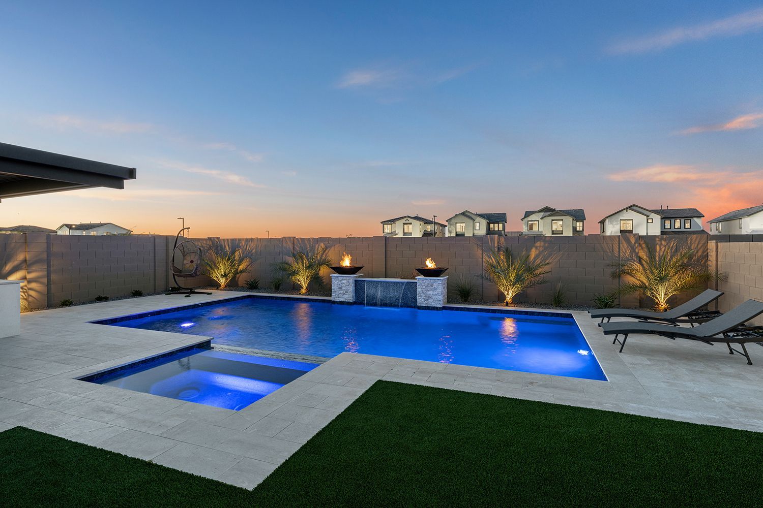Backyard pool with spa, fire features, lounge chairs, and artificial grass under a twilight sky.