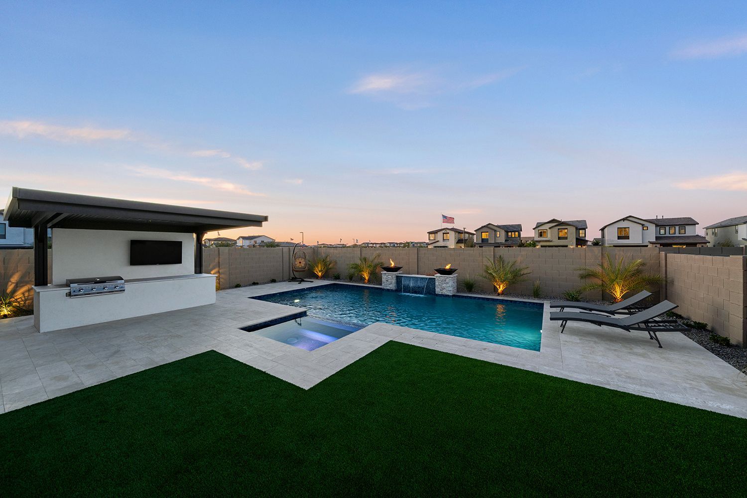 Backyard pool with a covered outdoor kitchen, lush lawn, and houses in the distance.