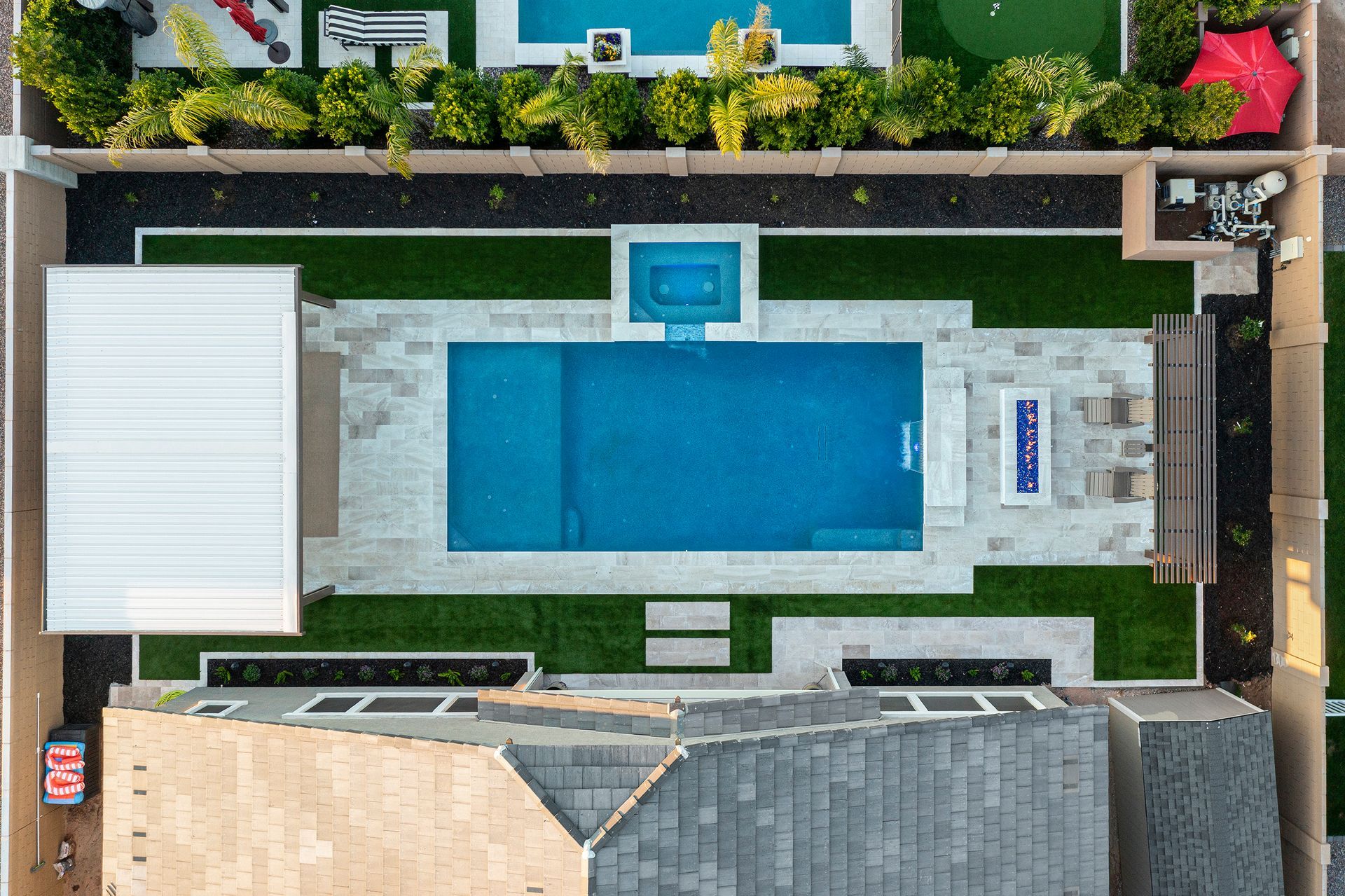 Overhead view of a backyard with a rectangular pool, hot tub, grass, patio, and modern architectural elements.